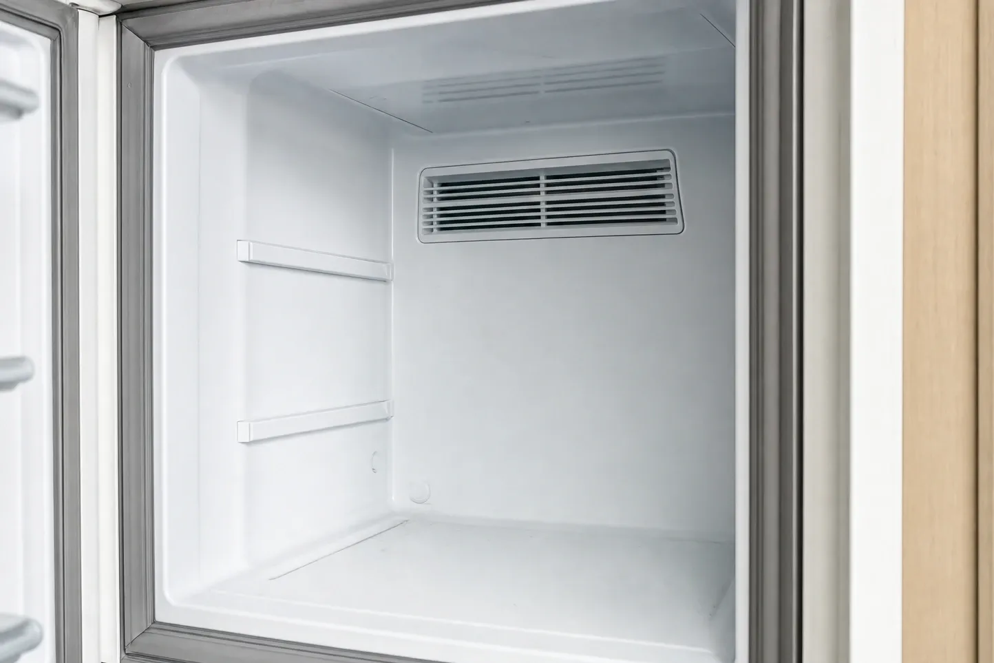 Empty white compartment with a single air-duct grille high on the rear wall and two shelf rails on the side wall