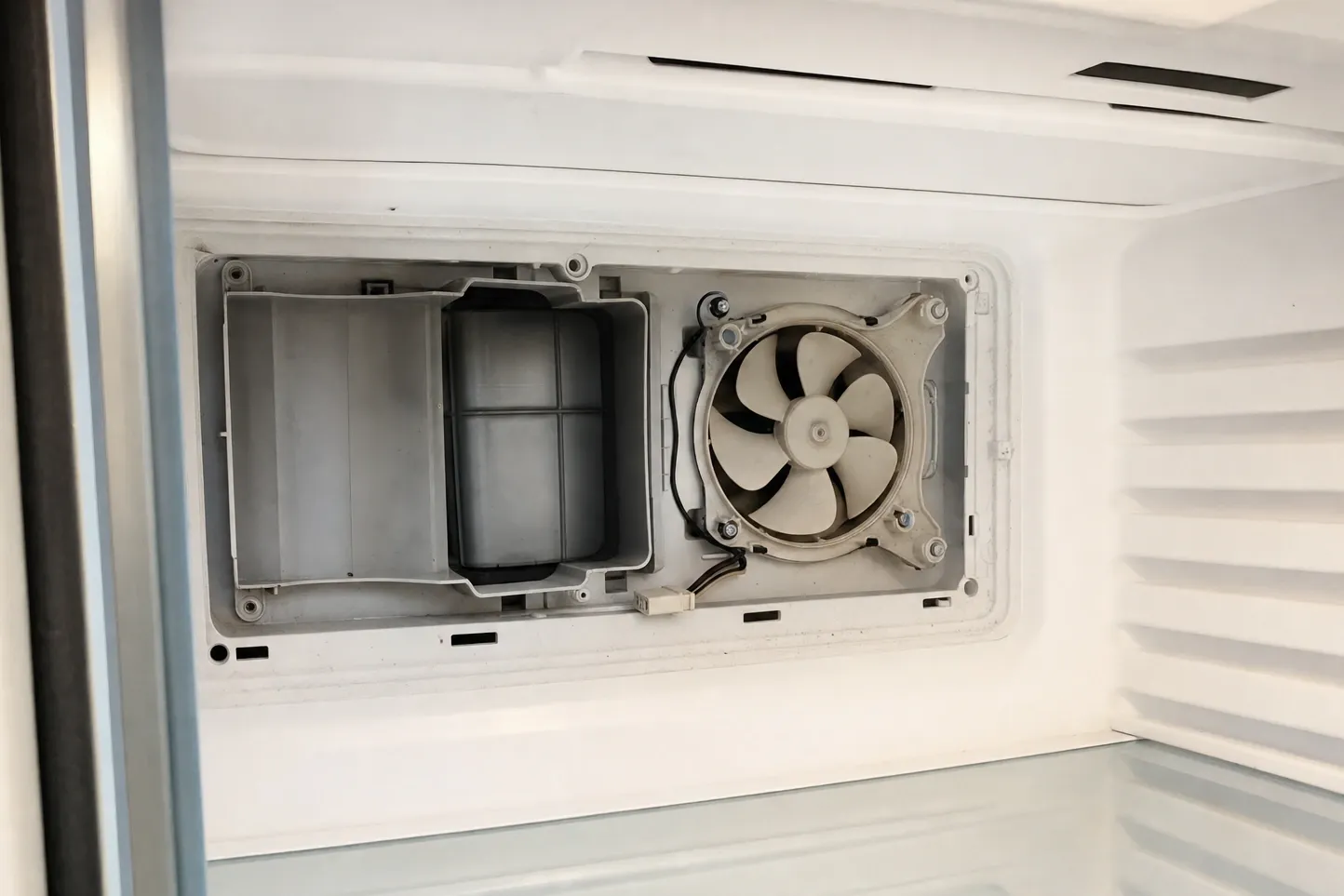 Evaporator fan and drain trough exposed behind the removed rear panel of a frozen compartment